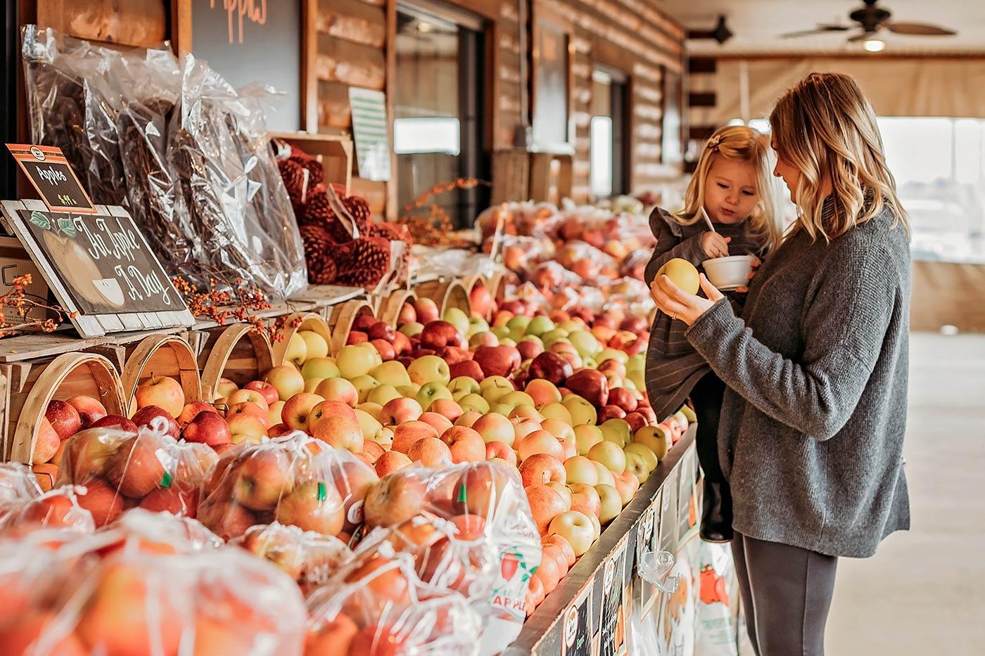 Mom and daughter shopping for apples at an outdoor fruit stand